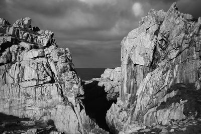 Rocks on cliff by sea against sky