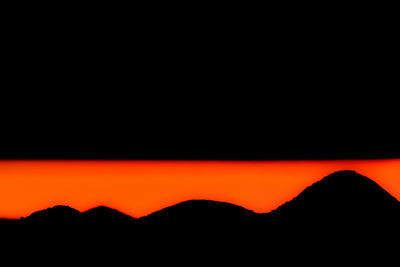 Scenic view of silhouette mountains against orange sky