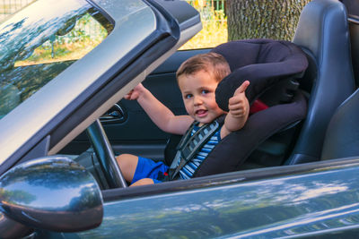 Boy showing thumb up while sitting in car