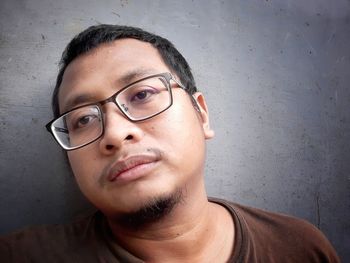Portrait of young man wearing eyeglasses against wall