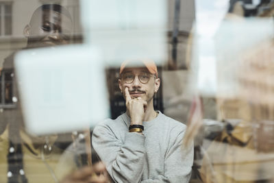 Thoughtful male programmer looking at adhesive notes on window at tech start-up office