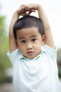 Portrait of cute boy with arms raised standing outdoors