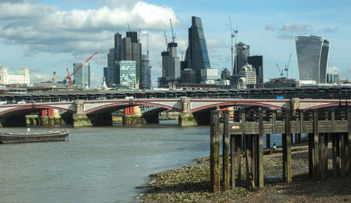 Bridge over river by buildings against sky in city