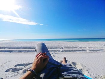 Low section of man relaxing on beach against blue sky