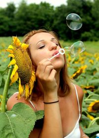 Young woman bowing bubbles on sunflower field