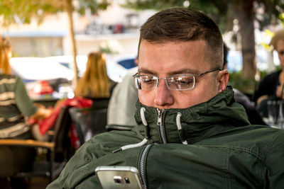 Close-up of young man using phone while sitting at outdoor cafe