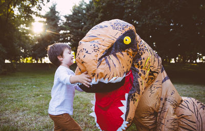 Boy embracing person wearing dinosaur costume in park