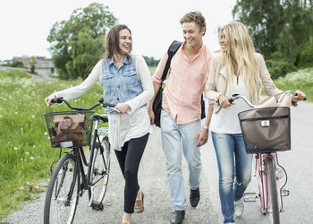 Young friends with bicycles walking on country road