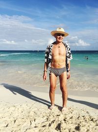 Portrait of man in sunglasses and hat standing at beach against sky