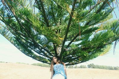 Young woman standing on tree at beach against sky