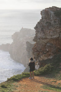 Rear view of man standing on rock by sea