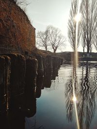 Reflection of bare trees in lake against sky