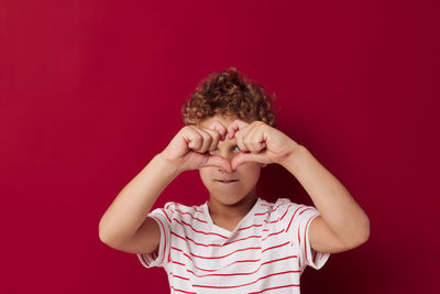 Boy making heart shape against red background