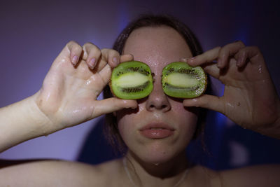 Close-up of woman covering eyes with kiwi slices in darkroom