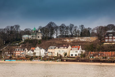 Houses by river and buildings against sky