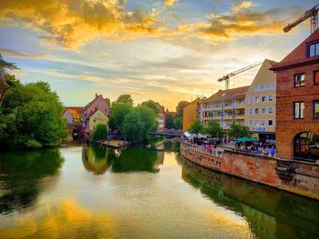 Buildings by river against sky during sunset