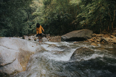 Man standing on rock by river in forest