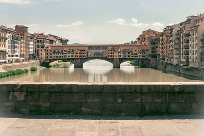 Arch bridge over river amidst buildings in city against sky