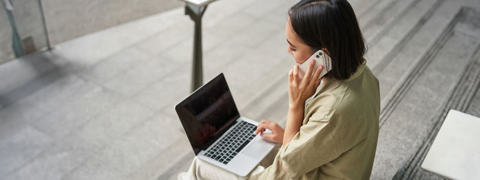 Rear view of young woman using laptop while standing in office