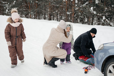 Family on a weekend in the snowy forest, dad prepares a sleigh for skiing