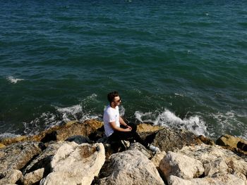 Full length of man sitting on rock in sea