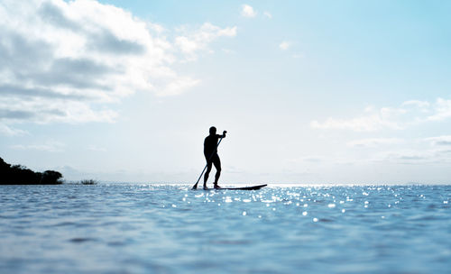 Silhouette man surfing in sea against sky