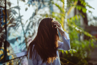 Young woman with tousled hair standing against plants