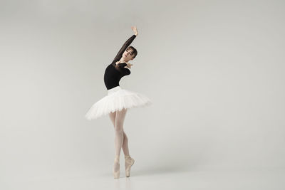 A ballerina in a bodysuit and tutu poses in motion showing ballet elements while standing on pointes