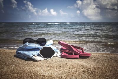 Close-up of shoes on beach against sky