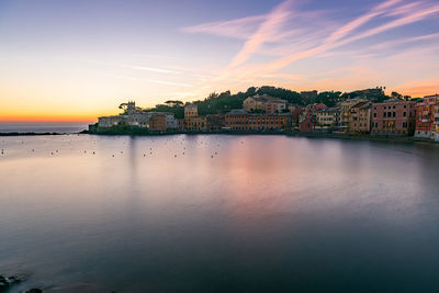 Scenic view of sea by buildings against sky during sunset