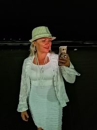 Woman wearing hat standing against black background