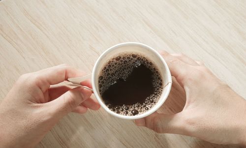 Close-up of hand holding coffee cup on table