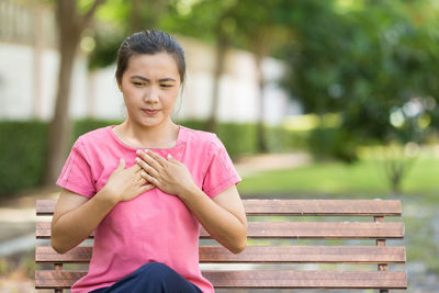 Young woman suffering from chest pain while sitting on bench at park