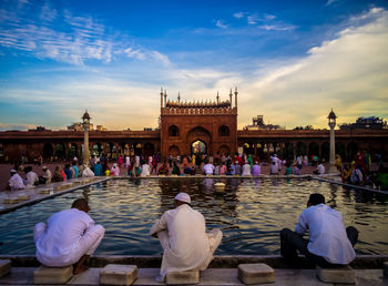 People resting at delhi jama masjid mosque against sky during sunset