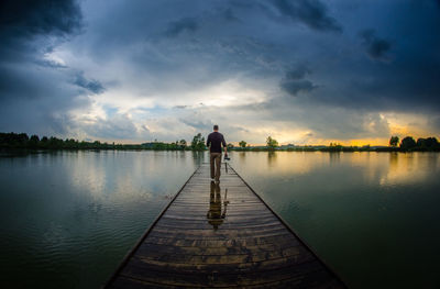 Man walking on jetty by lake against sky