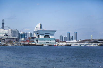 Modern buildings in front of river against blue sky on sunny day at harbor