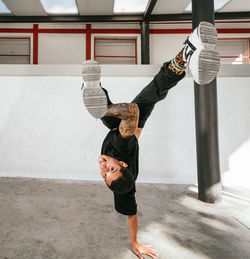Full body of energetic young man doing acrobatic handstand while performing break dance