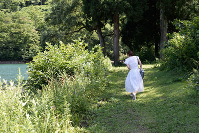 Rear view of woman walking on field by trees
