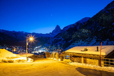 Illuminated road by snowcapped mountains against blue sky at night