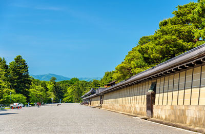 Road amidst trees and buildings against blue sky