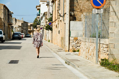 Rear view of woman walking on street amidst buildings