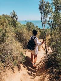 Rear view of woman walking by sea against sky