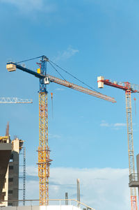 Low angle view of cranes at construction site against sky