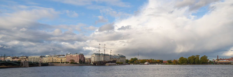 Panoramic view of buildings by sea against cloudy sky