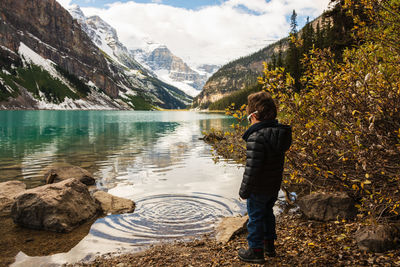 Rear view of boy standing by lake against mountains