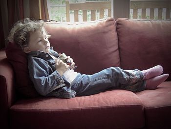 Side view of boy holding cup while relaxing on sofa at home