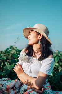 Side view of woman looking away while standing against sky