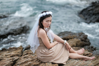 Side view of woman sitting on rocky shore