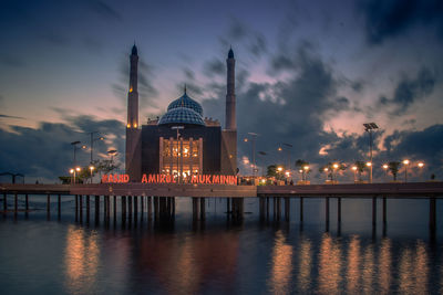 Illuminated temple by building against sky during sunset