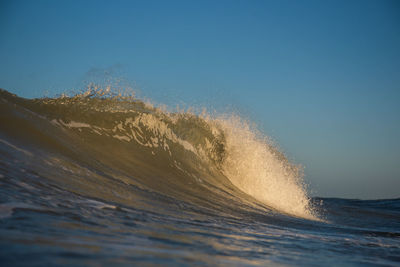 Sea waves splashing on shore against clear blue sky